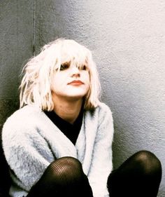 a woman with blonde hair sitting on the floor wearing black tights and a white coat