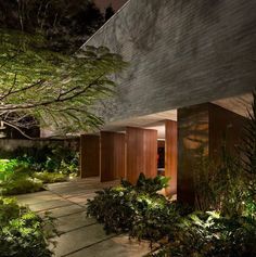 an exterior view of a house at night with lights on and plants in the foreground