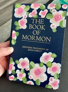 the book of mormon is being held up by someone's hand with flowers painted on it