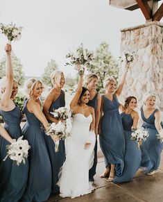 a group of women standing next to each other in front of a stone wall holding bouquets