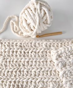 a white crochet blanket with a ball of yarn next to it