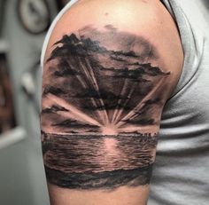 a man's arm with a black and grey sunset tattoo on the upper half of his arm