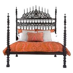 an ornate iron bed frame with orange and white pillows