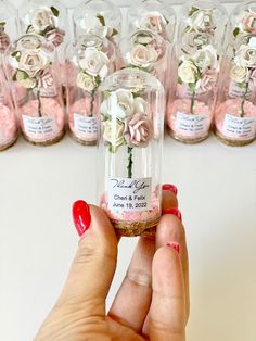 a hand holding a tiny jar with flowers in it next to some jars filled with pink and white roses