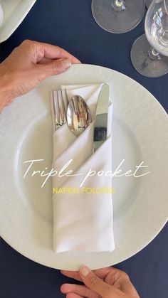 two hands holding silverware on top of a white plate with napkins and wine glasses