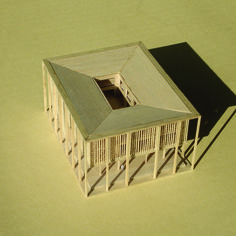 a wooden model of a house with a roof and windows on the top floor, in front of a green background