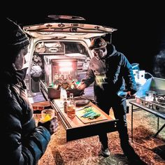 two men standing in front of an open van with food and drinks on the table