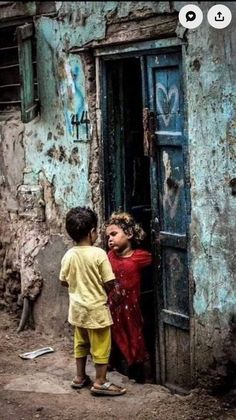 two children are standing in the doorway of an old building that has graffiti on it