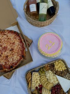 a table topped with pizza, cheese and crackers next to bottles of wine on top of a white table cloth