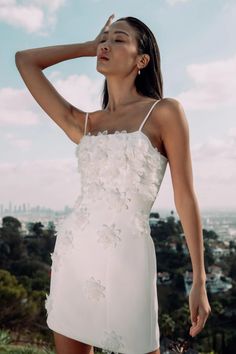 a woman in a white dress standing on top of a hill with her hands behind her head