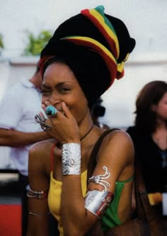 a woman with tattoos on her arm holding a cell phone to her ear and wearing a colorful hat