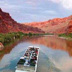 a large boat traveling down a river surrounded by red rocks and water with people on it