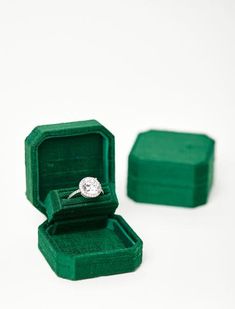 an open ring box with a diamond in it on a white surface, next to a green velvet case