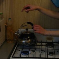 two hands are reaching for a tea kettle on the stove top, while another person holds out their hand