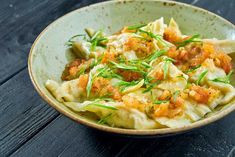 a bowl filled with pasta and vegetables on top of a wooden table next to a fork