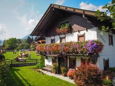 a house with flowers on the balconies and people in the back yard outside