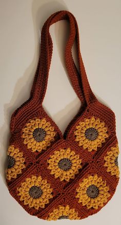 an orange crocheted bag with yellow and brown flowers on the front, sitting on a white surface