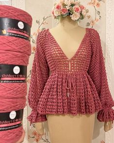 a mannequin wearing a pink crochet top next to two balls of yarn