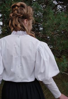 a woman in a white shirt and black skirt standing next to some pine tree branches