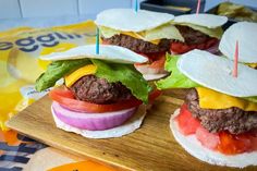 hamburgers with lettuce, tomato and cheese on a cutting board next to chips