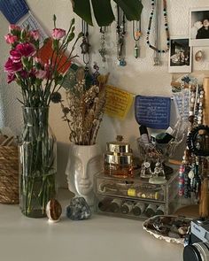 a white table topped with lots of jewelry and vases filled with flowers next to a camera