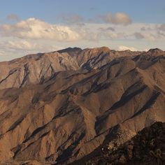 the mountains are brown in color with some white clouds above them and blue sky over them