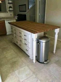 a kitchen island made out of white cabinets and drawers with a trash can underneath it