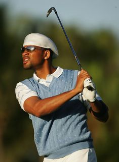 a man in blue shirt and white cap holding a golf club with his right hand