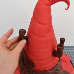 a hand is holding the top of a fake red wizard's hat on a cake