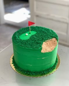 a cake with green frosting and a red golf flag on top is sitting on a table