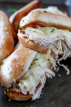 three sandwiches with meat and cheese on them sitting on a black plate next to bread sticks