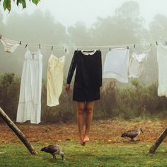 a woman is standing in front of clothes hanging on a line and two birds near by