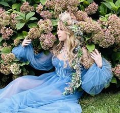 a woman in a blue dress sitting on the ground with flowers around her neck and hands behind her head