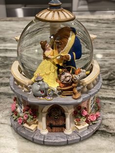 the figurine is sitting on top of the snow globe with beauty and the beast characters