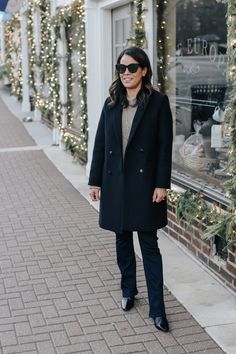 Woman wearing navy coat with dark jeans, boots, brown sweater standing against outside facade of building. Parisian Wardrobe, French Clothing, Fall Winter Jacket, Parisian Women, French Outfit, Navy Coat