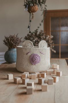 a crocheted basket with a pig face on it and wooden blocks scattered around