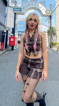 a woman with pink hair and makeup is standing on the street in front of an arch