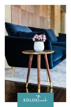 a small table with flowers on it in front of a blue couch and wooden wall