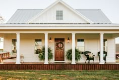 a white house with columns and plants on the front porch is featured in this image