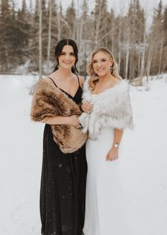 two women standing next to each other in the snow wearing fur stolers and dresses