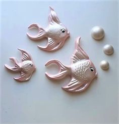 three pink plastic fish with pearls on a white surface