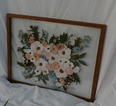 an image of a flower arrangement in a frame on a white sheeted bed spread