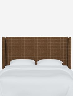 an upholstered headboard on a bed with white sheets and brown checkered pillows