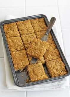 a pan filled with squares of food on top of a white tile counter next to a knife