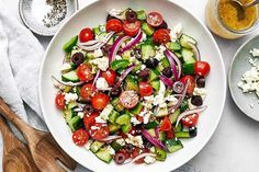 a salad with cucumbers, tomatoes, olives and feta cheese in a white bowl