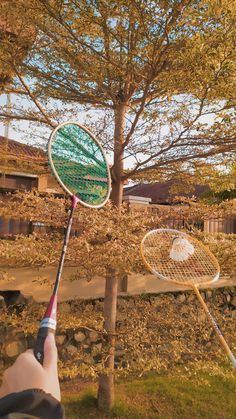 a person holding a tennis racquet in front of a tree and another racket