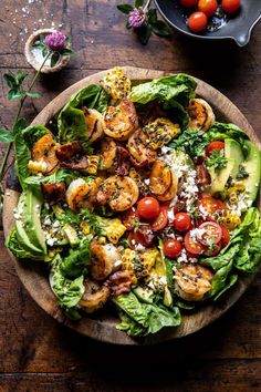 a salad with shrimp, lettuce and tomatoes in a bowl on a wooden table