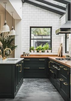 a kitchen with black cabinets and white brick walls is pictured in this image, there are potted plants on the counter