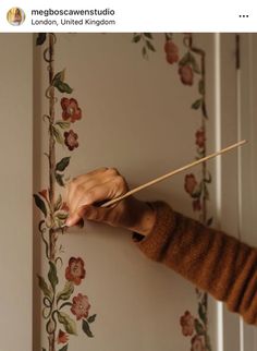 a person holding a stick in front of a flowered wall