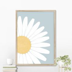 a white and yellow flower on a blue background in a wooden frame next to some books